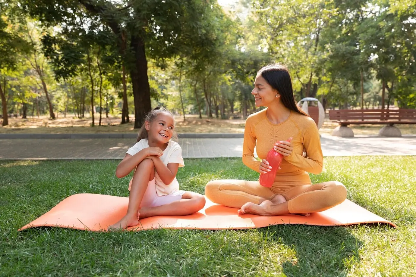 Ganzkörperaufnahme einer lächelnden Frau und eines Kindes auf einer Matte.